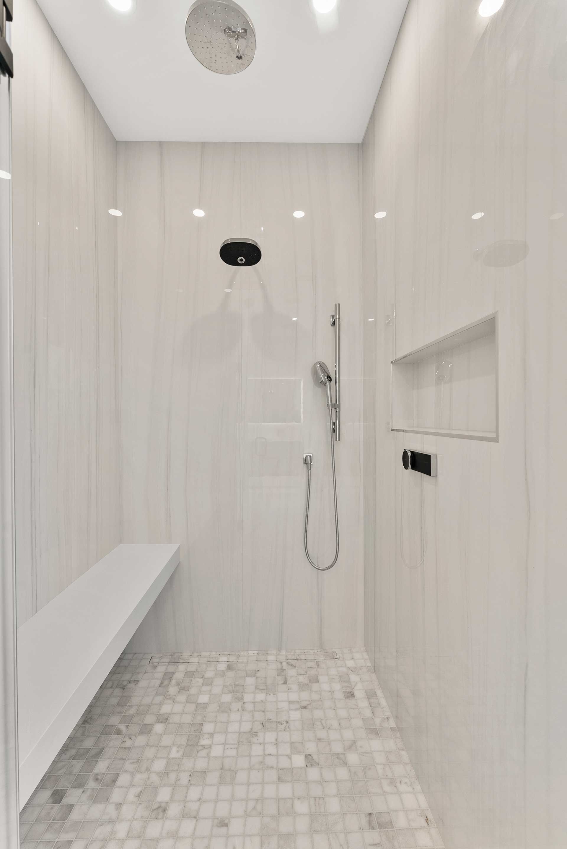 Modern white tiled shower with a built-in bench, showerheads, and a tiled floor.