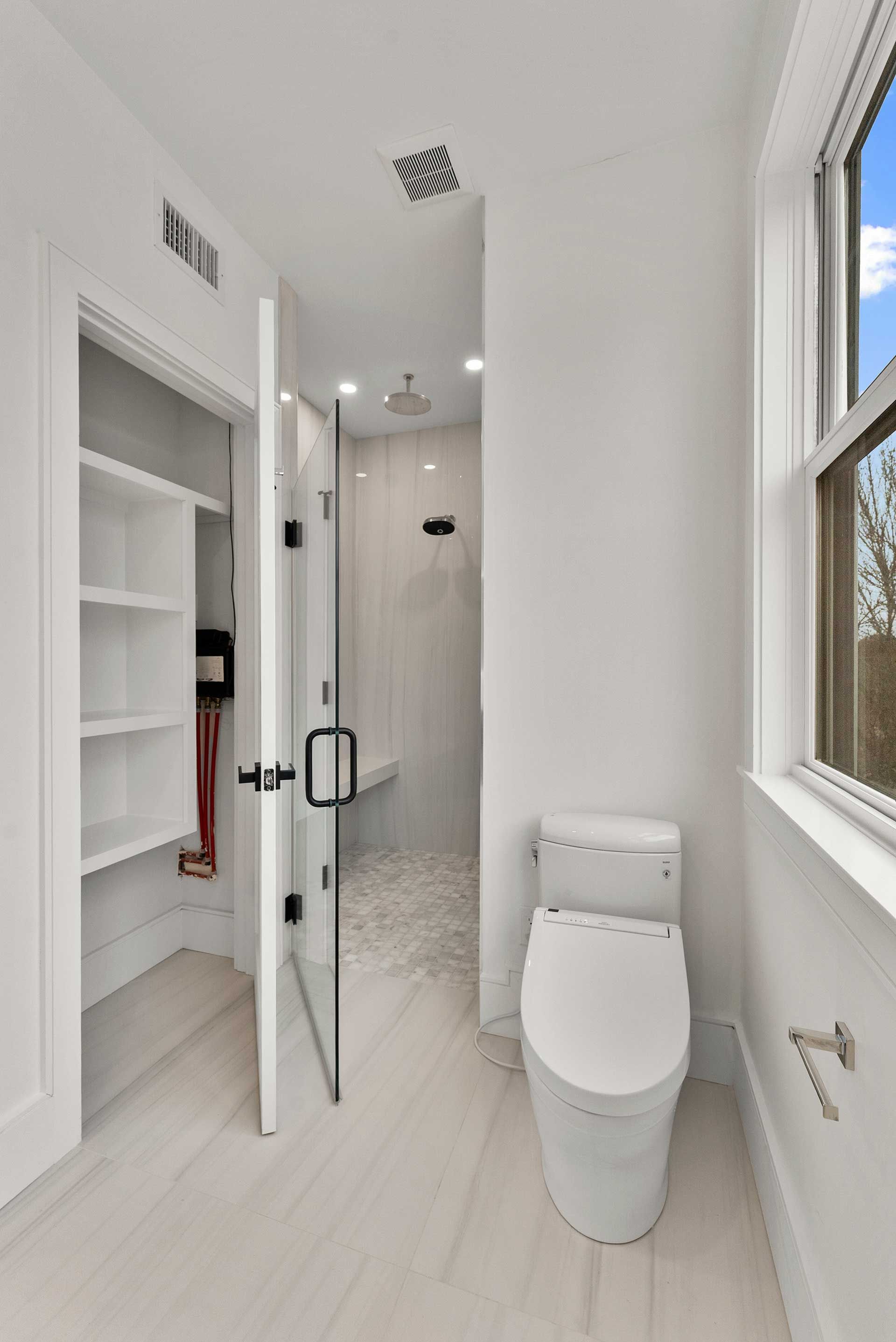 A narrow, all-white bathroom with a walk-in shower, toilet, and closet.