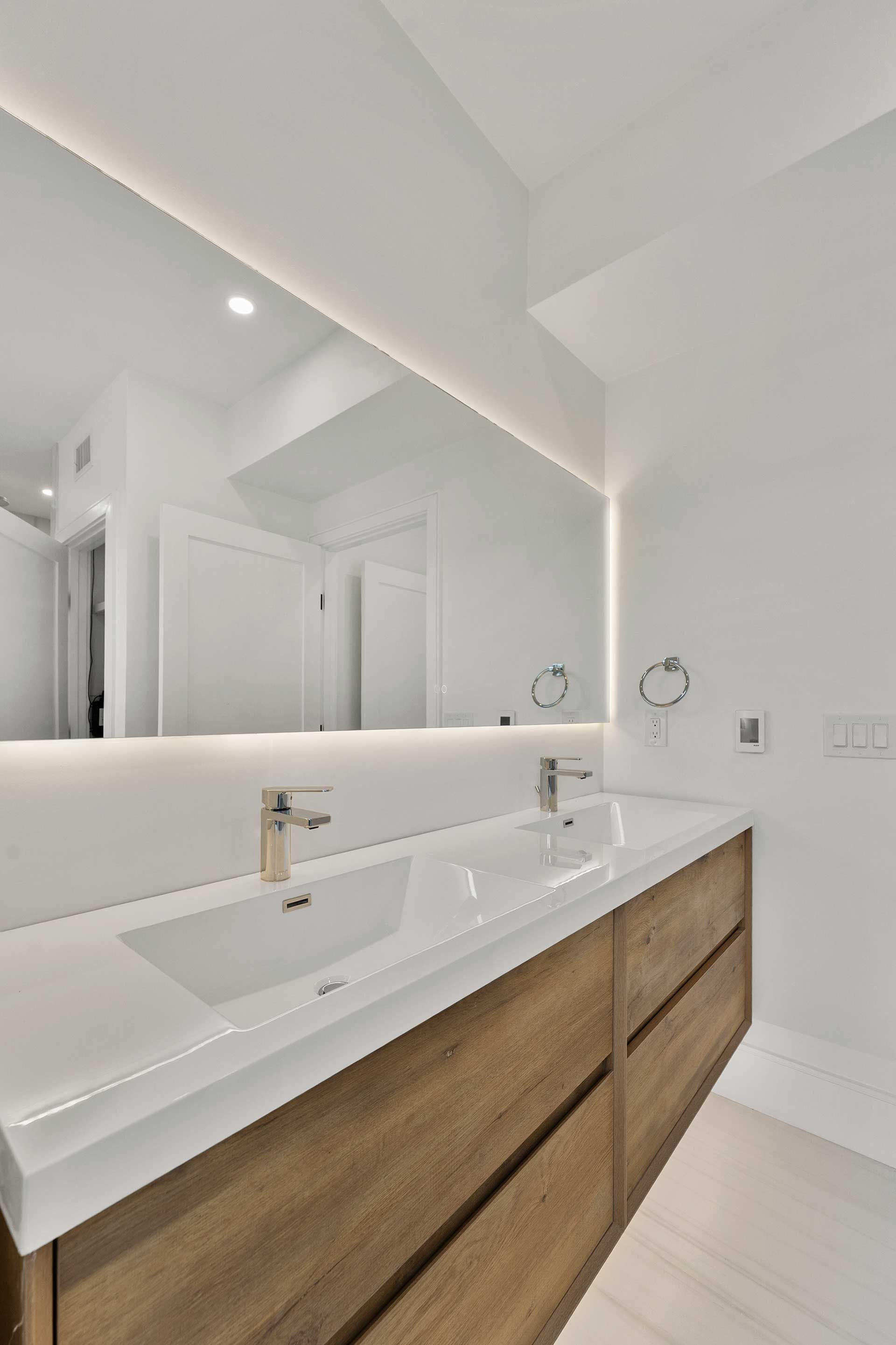 Modern bathroom with a long wooden vanity, double sinks, and a large mirror with LED lighting.
