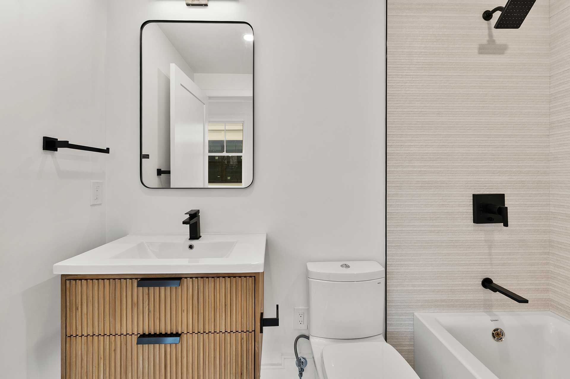 Modern bathroom with light wood vanity, white walls, and a tiled shower wall.