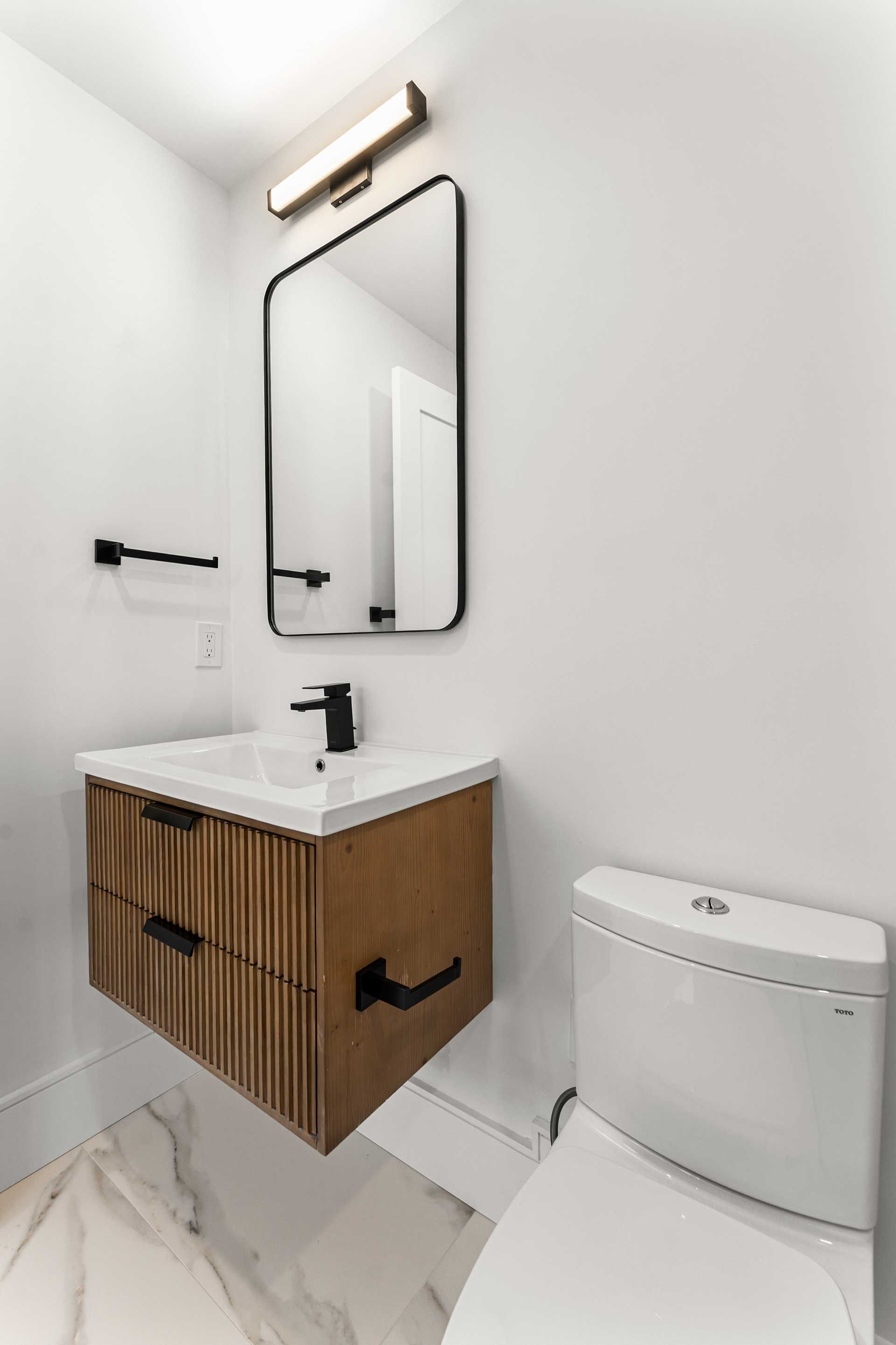 Small modern bathroom with a floating wood vanity, black fixtures, and a rectangular mirror.