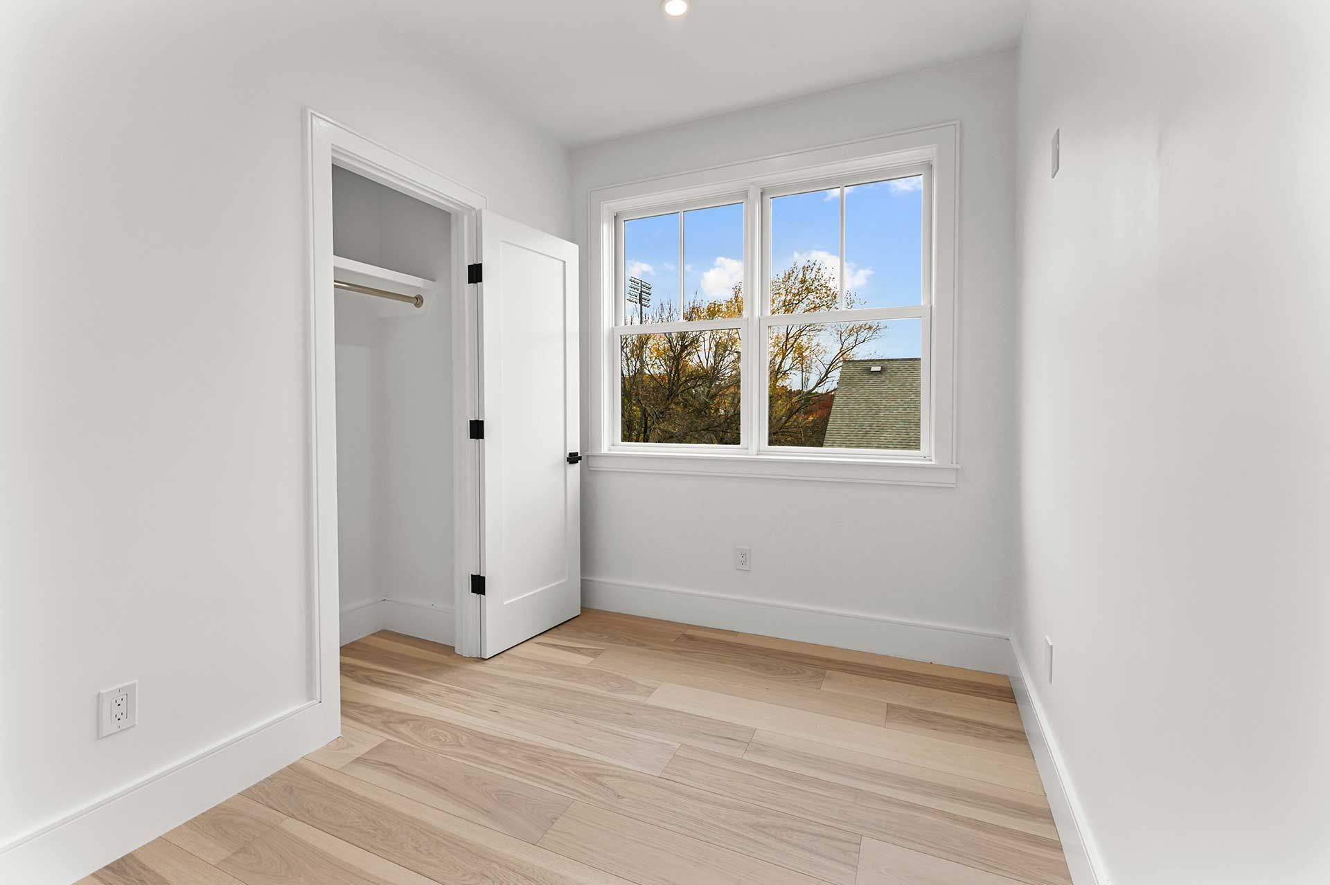 Empty, bright bedroom with open closet, window, and hardwood floor.
