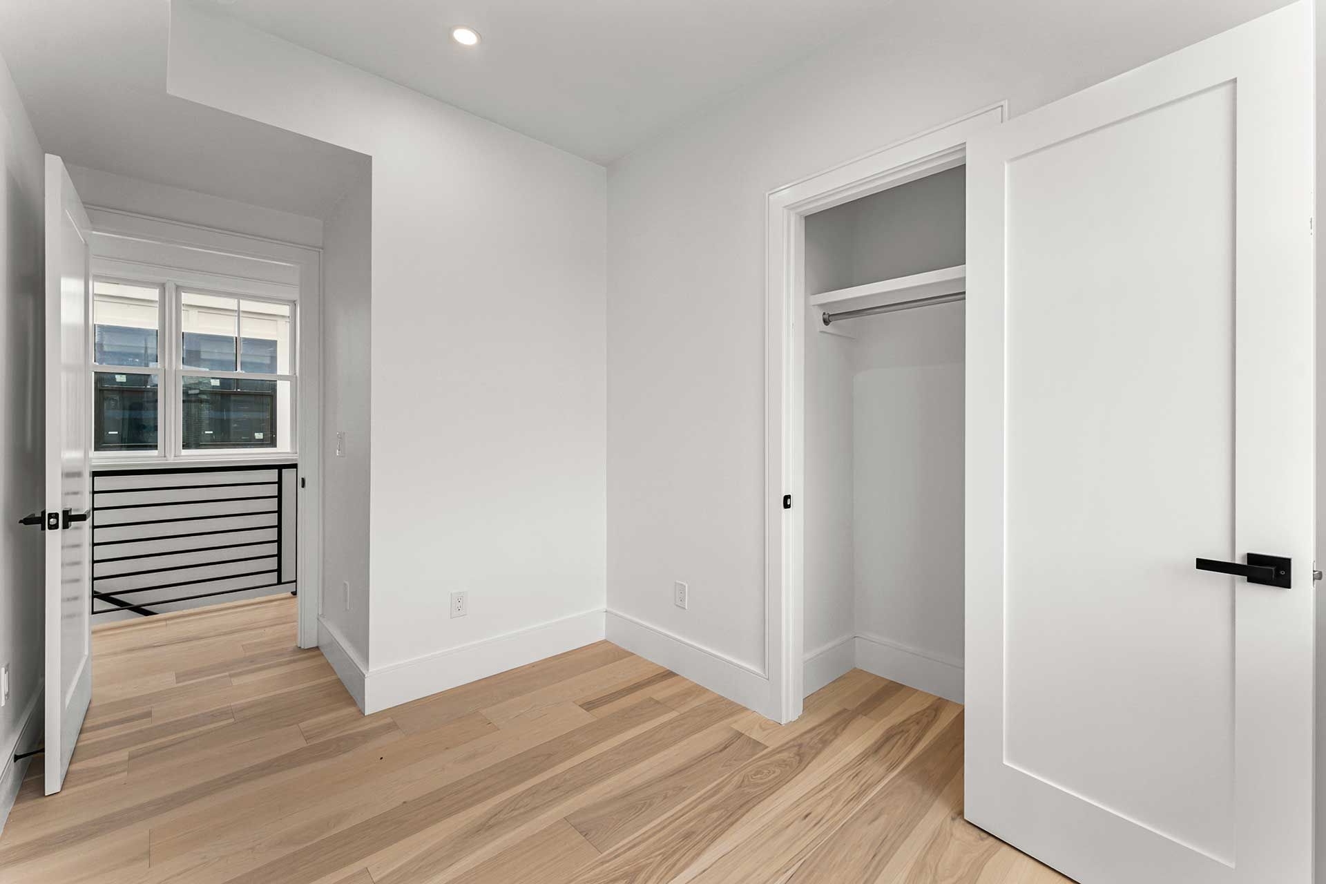 Empty room with hardwood floors, closet, and doorway leading to a sunlit balcony.