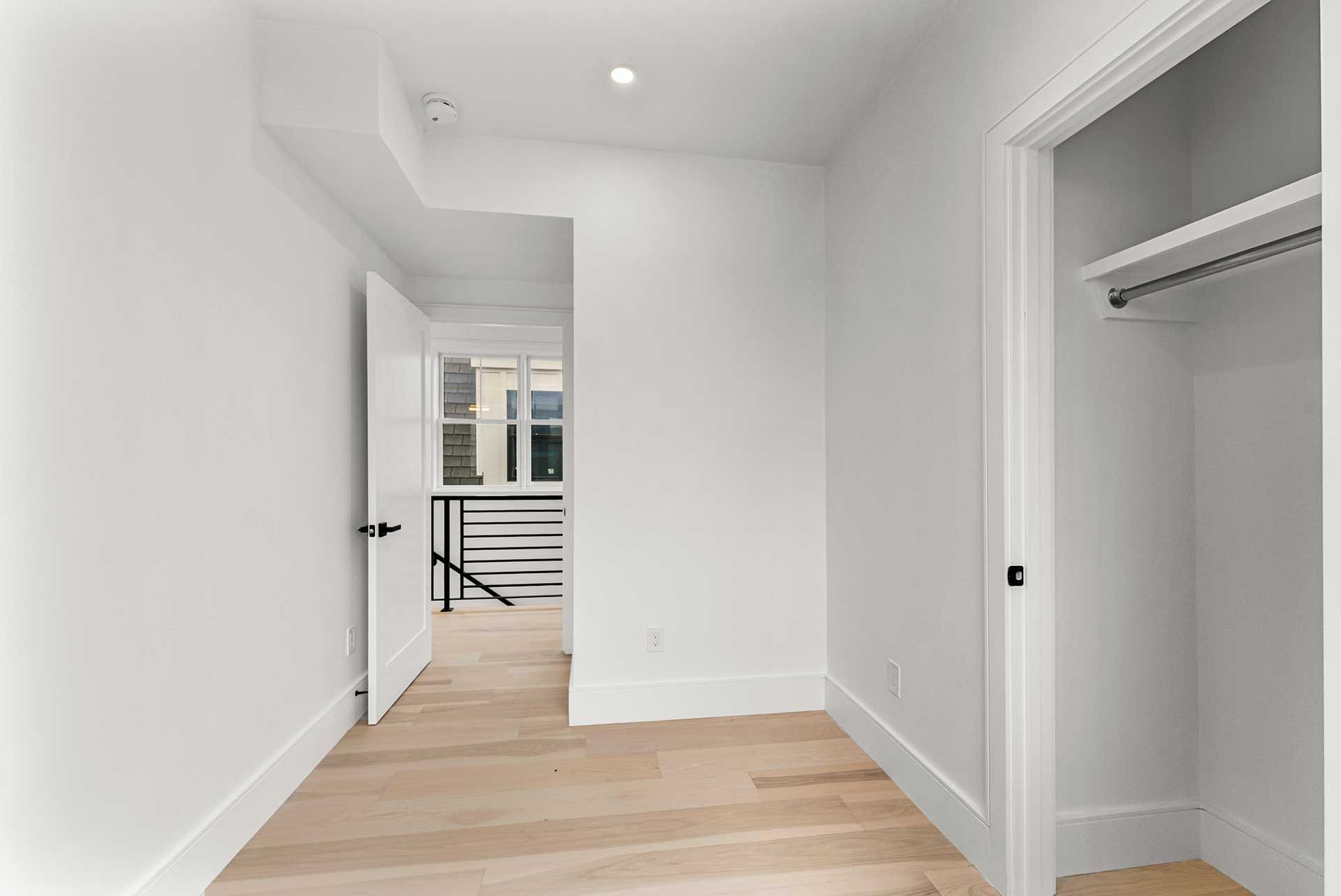 Empty hallway with white walls and wood floor, closet on right, doorway ahead.
