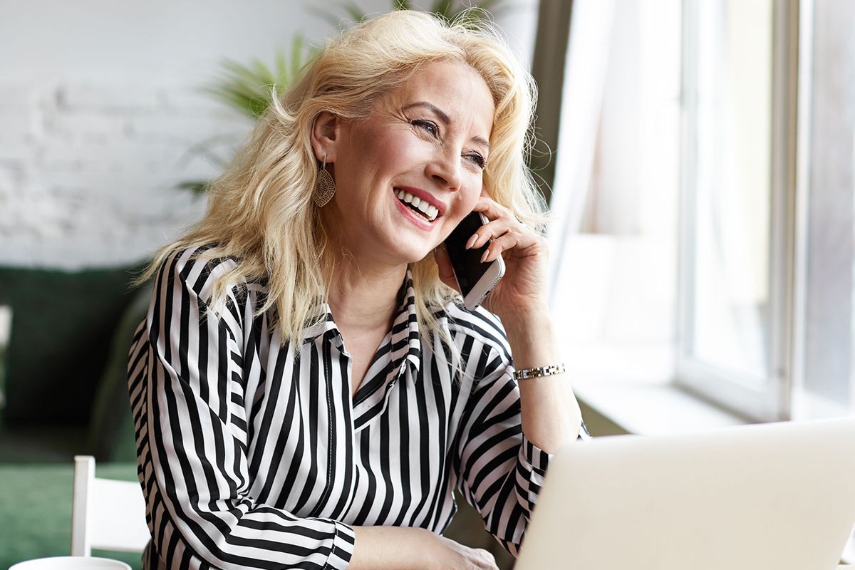 A woman is sitting in front of a laptop computer talking on a cell phone.