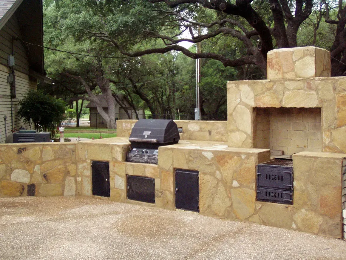 A stone wall with a grill and a fireplace built into it