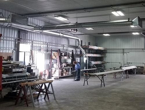 Large industrial workshop with metal tables, machinery, and a person standing near the back wall.