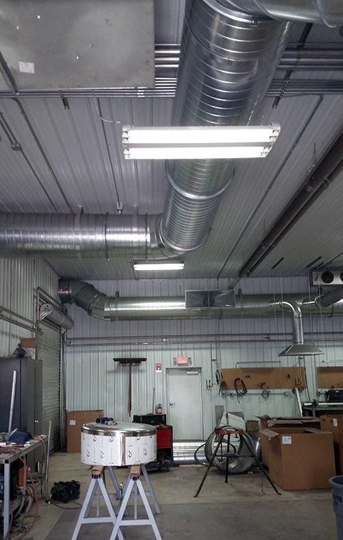 Industrial workshop interior with exposed ducting, fluorescent lights, and tools on tables against the wall