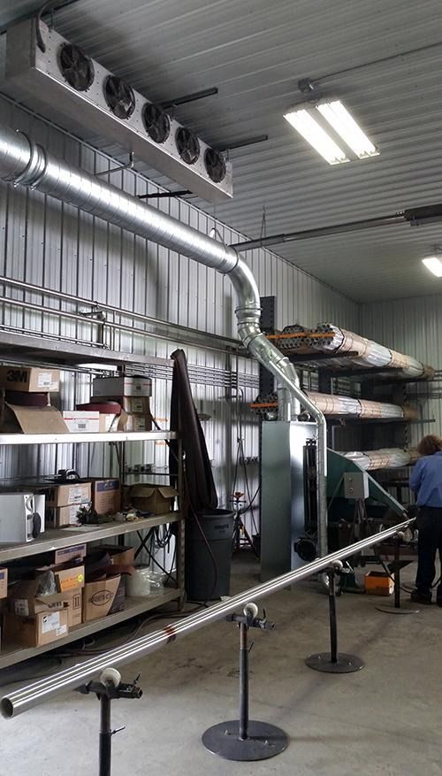 Industrial kitchen or storage room with metal shelving, ductwork, and a person working near equipment