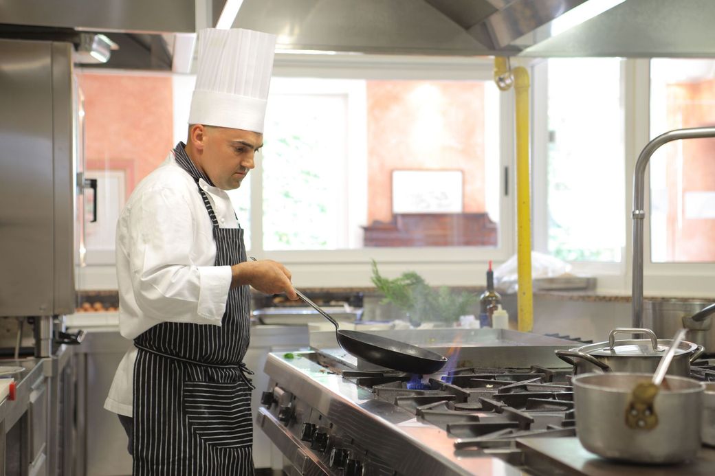 Chef cooking at a stainless steel stove in a bright restaurant kitchen