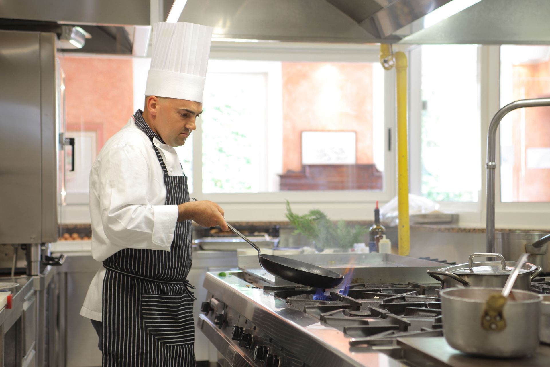 Chef cooking at a stainless steel stove in a bright restaurant kitchen