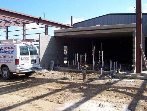 Construction site with partially built garage, utility truck, and exposed pipes in front of a dark opening