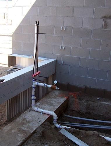 Indoor utility area with exposed white pipes, a red valve, and a concrete block wall.