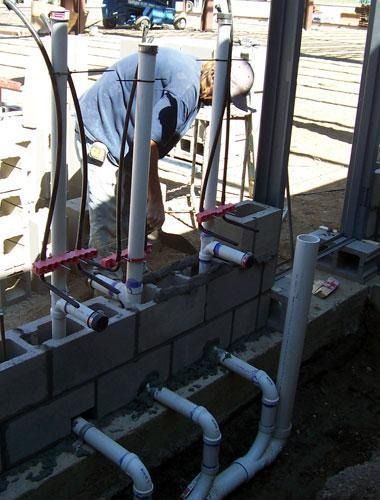 Worker inspecting plumbing at a construction site beside a cinderblock wall