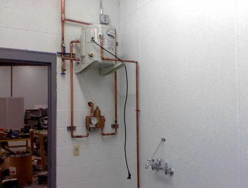 Wall-mounted boiler and copper piping in a utility room beside a sink and open doorway.