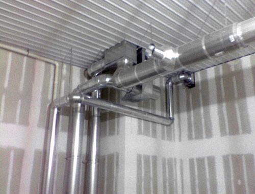 Industrial ductwork and metal pipes installed in a room with unfinished drywall walls and a corrugated ceiling