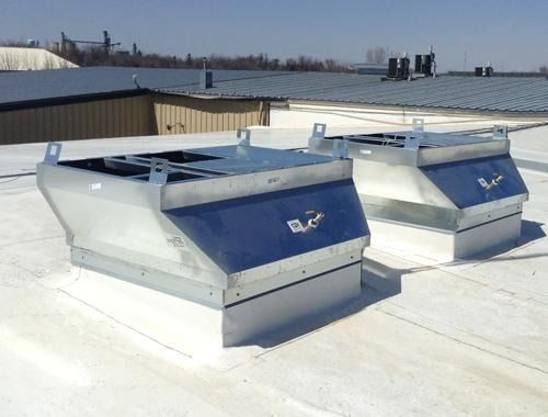 Two silver rooftop ventilation units with blue panels on a flat white rooftop under a clear sky