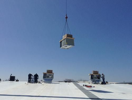 Crane lowering a small structure onto a snowy rooftop under a clear blue sky, with workers nearby