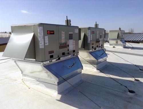 Row of rooftop HVAC units on a flat white roof under clear sky