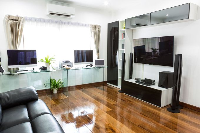 Modern living room with glossy wooden floor, black sofa, glass desk, and large TV wall unit