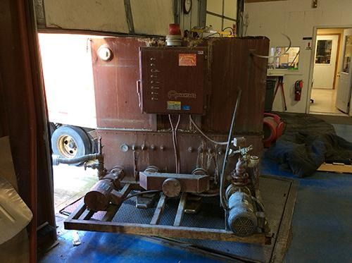 Large brown industrial machine with pipes and gauges in a workshop floor area