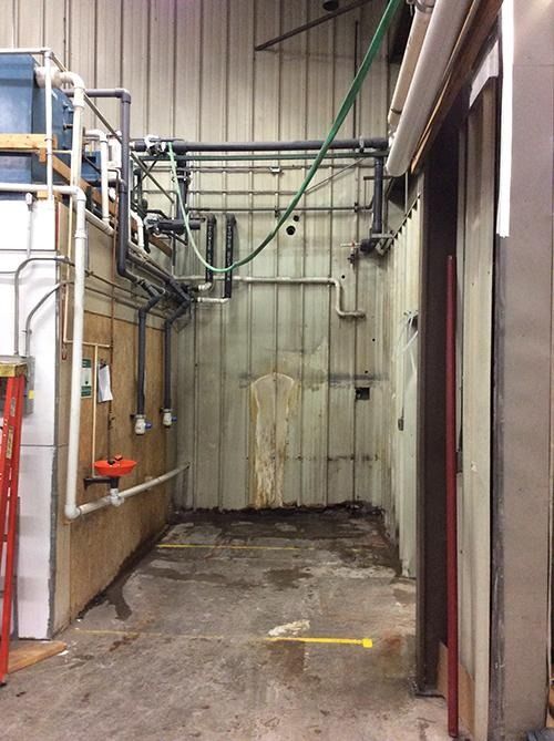 Narrow industrial alley with pipes, cables, and a concrete floor in a warehouse corridor