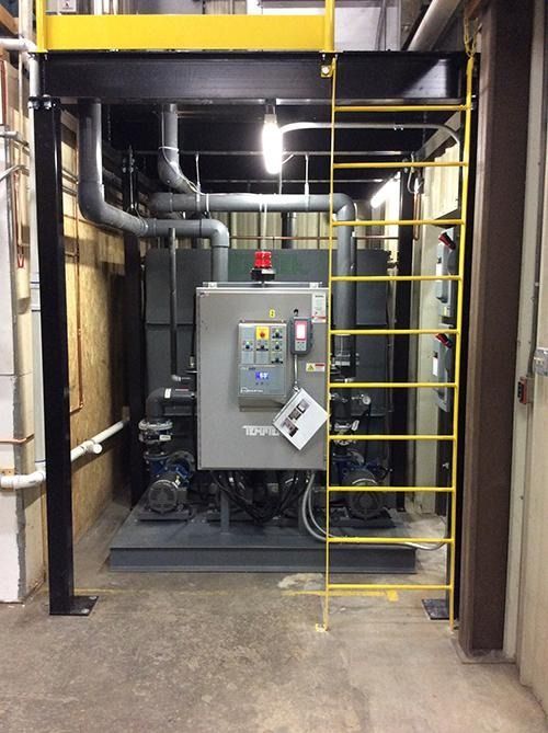 Industrial boiler room with gray machinery, yellow ladder, and pipes in a narrow utility corridor