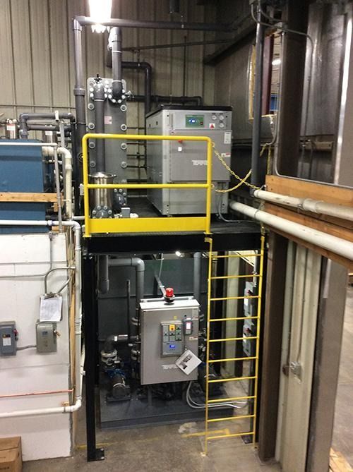 Industrial equipment on a metal platform with yellow railings and a ladder in a utility room.