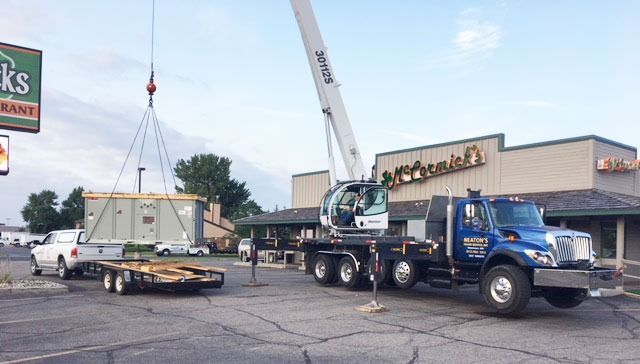Crane lifting a flatbed trailer in a parking lot outside a store.