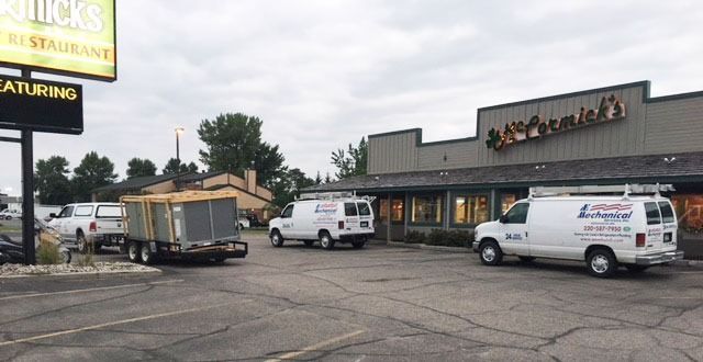 Parking lot outside a restaurant with two white service vans and a trailer under an overcast sky