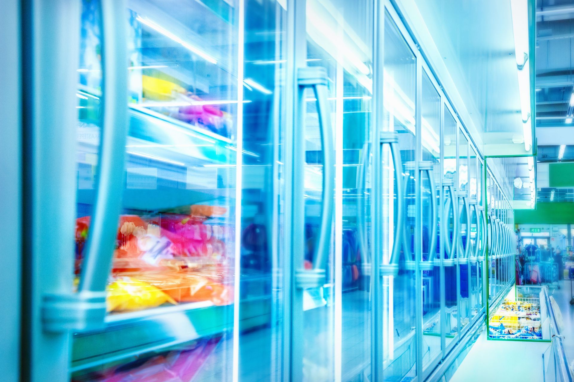 Bright modern supermarket aisle with glass refrigerator doors and colorful packaged food inside