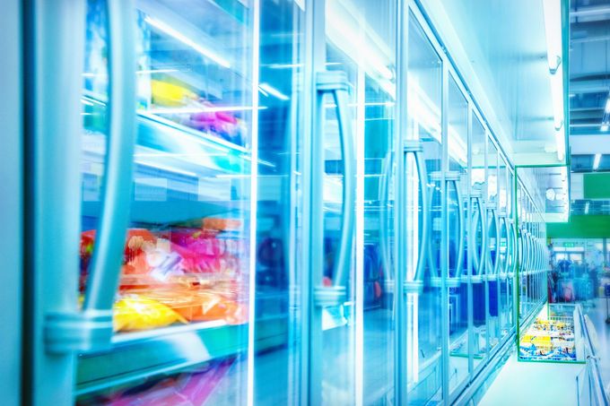 Bright modern supermarket aisle with glass refrigerator doors and colorful packaged food inside