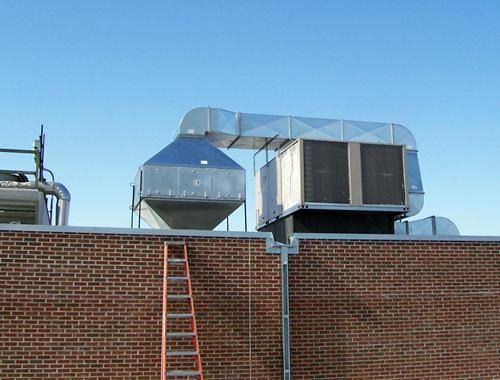 Rooftop HVAC units and silver ductwork above a brick wall, with a ladder leaning against it.