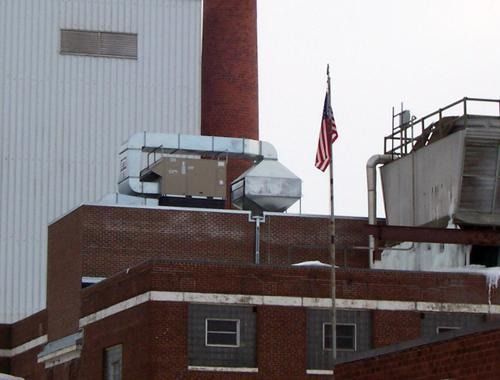 Rooftop HVAC equipment beside a U.S. flag on a brick industrial building