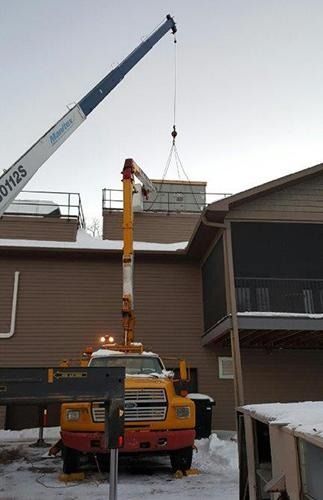 Crane lifting a rooftop HVAC unit onto a building, with a yellow utility truck below.