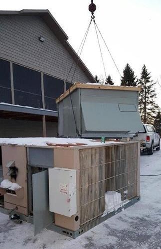 Crane lifting a small prefab room onto a snowy driveway beside a house