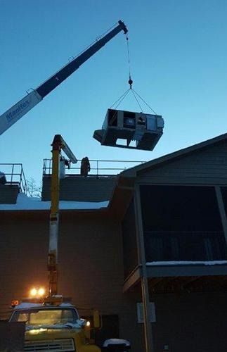 Crane lifting a small cabin-like structure above a building at dusk