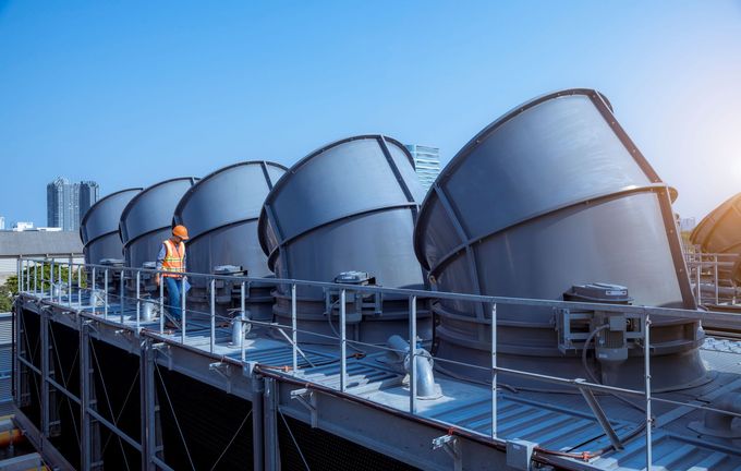 Industrial rooftop with large silver ventilation ducts and a worker in orange safety gear at sunrise