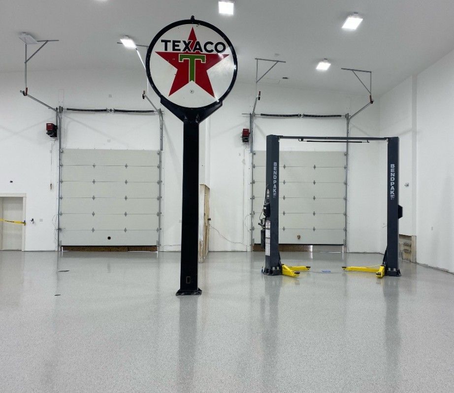 An empty auto shop interior with a Texaco sign, garage doors, and a car lift. The floor is polished concrete.
