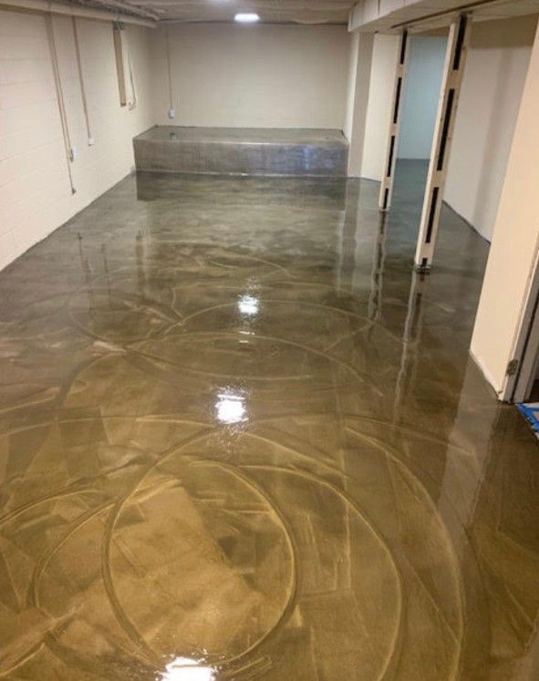 A basement with a shiny, metallic-looking epoxy floor reflecting light. The room has white walls and a rectangular area.