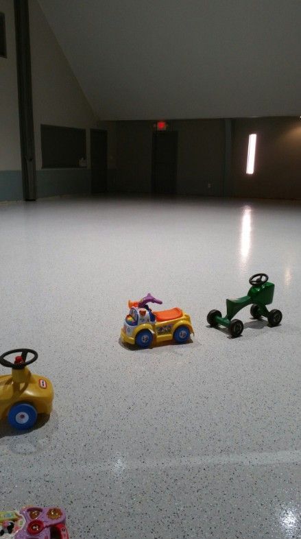 Toy cars of various styles are on a large, shiny, speckled floor in a room with an arched ceiling.