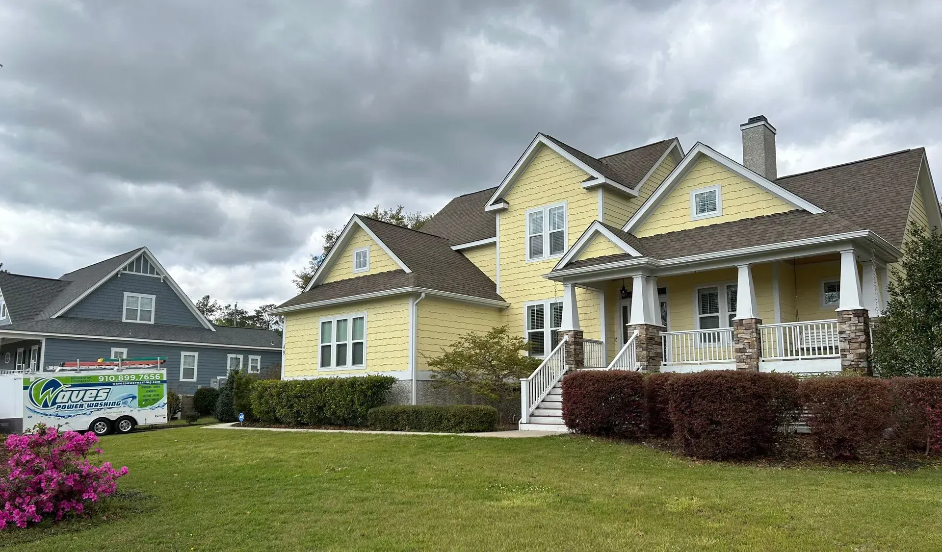 Yellow house with porch, brown roof, and dark cloudy sky.