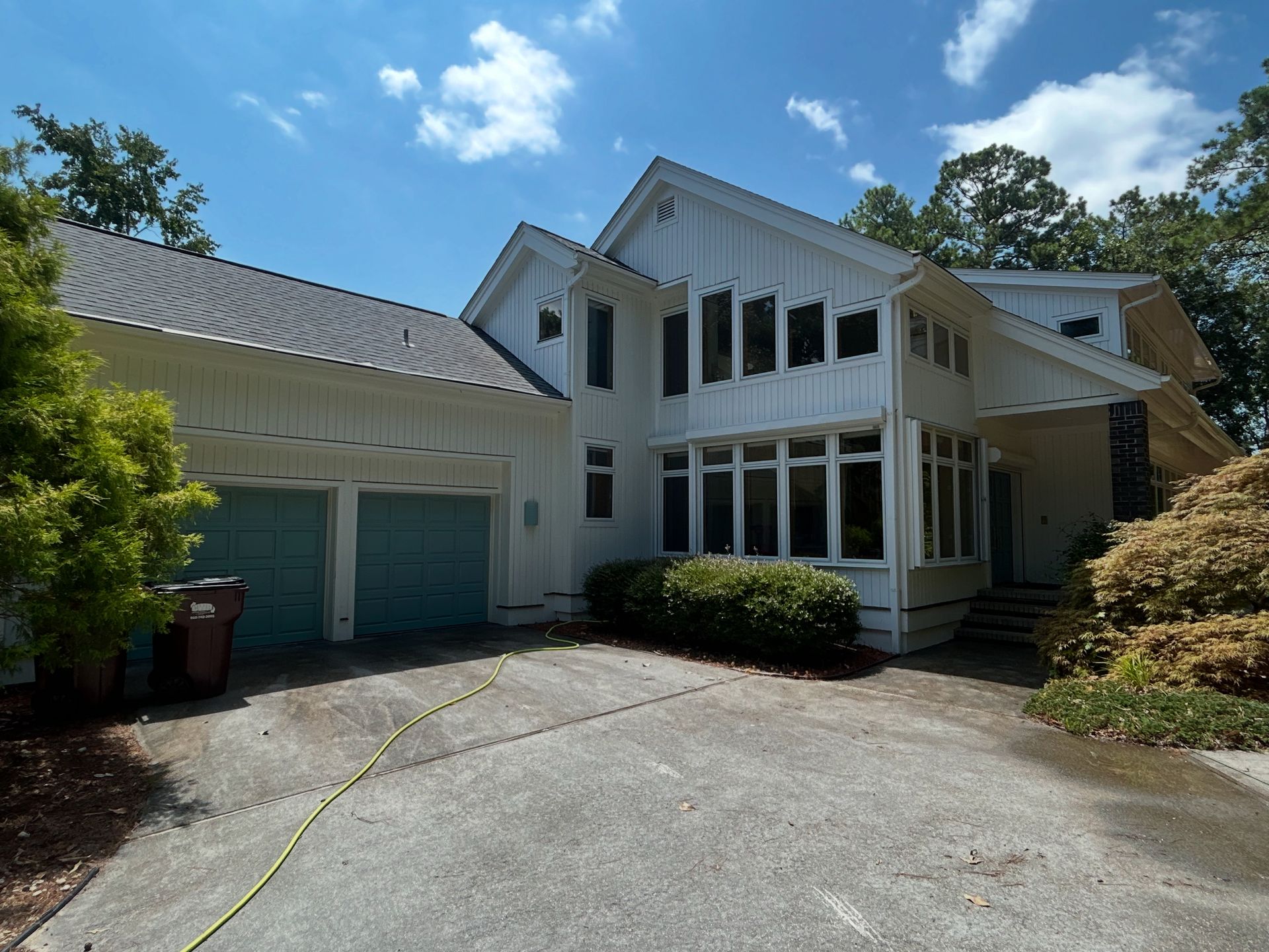 White house with teal garage doors, large windows, and a driveway on a sunny day.