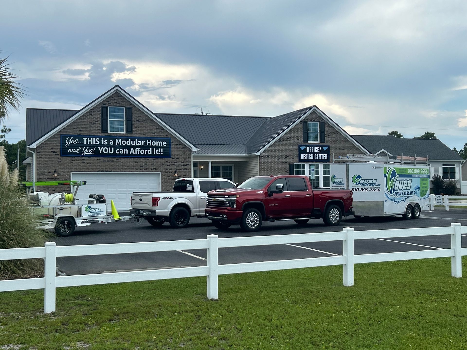 Building with black sign, trucks parked in front, white fence in foreground, cloudy sky.