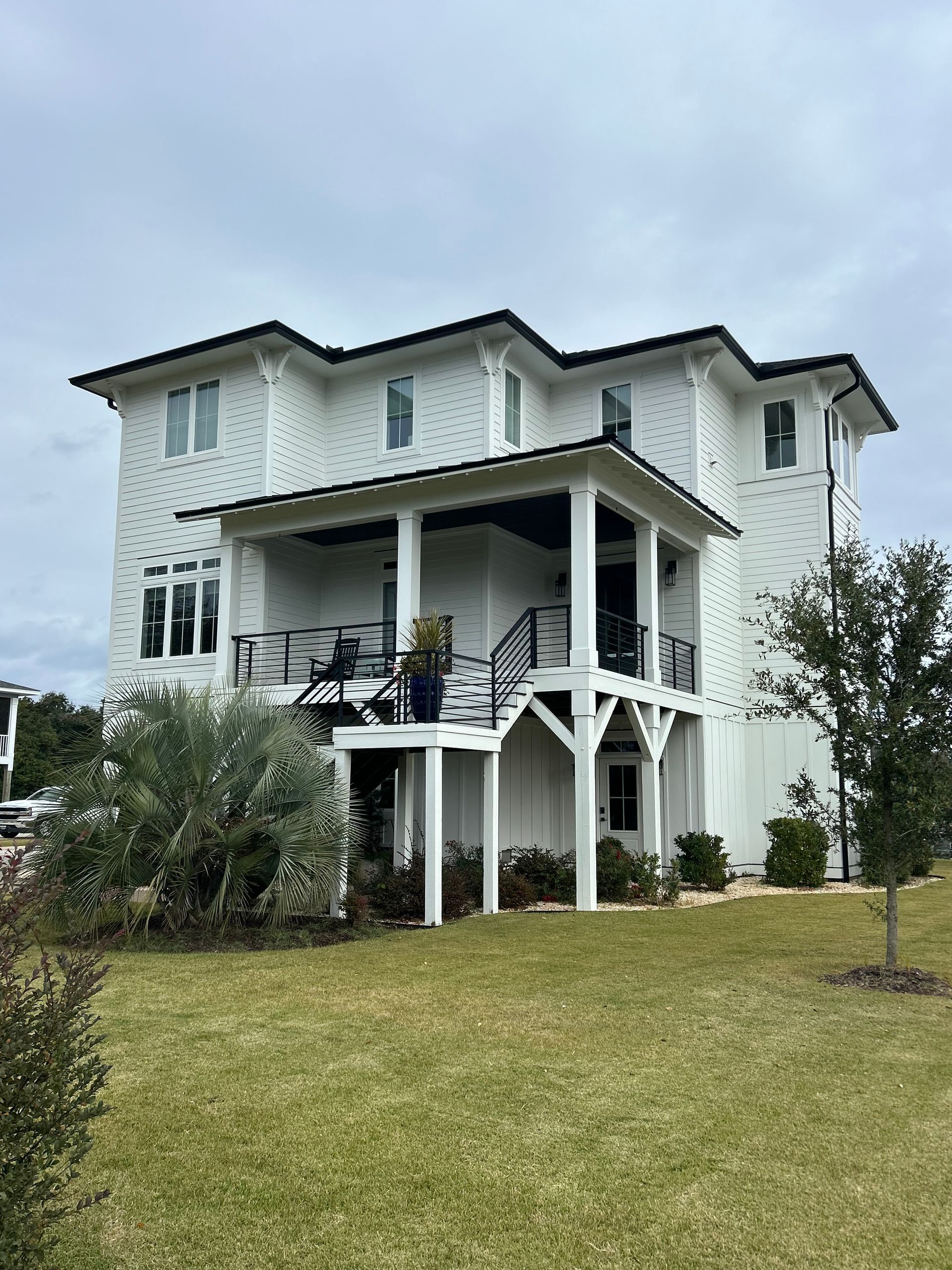 White two-story house with black trim, a covered porch, and a grassy yard under a cloudy sky.