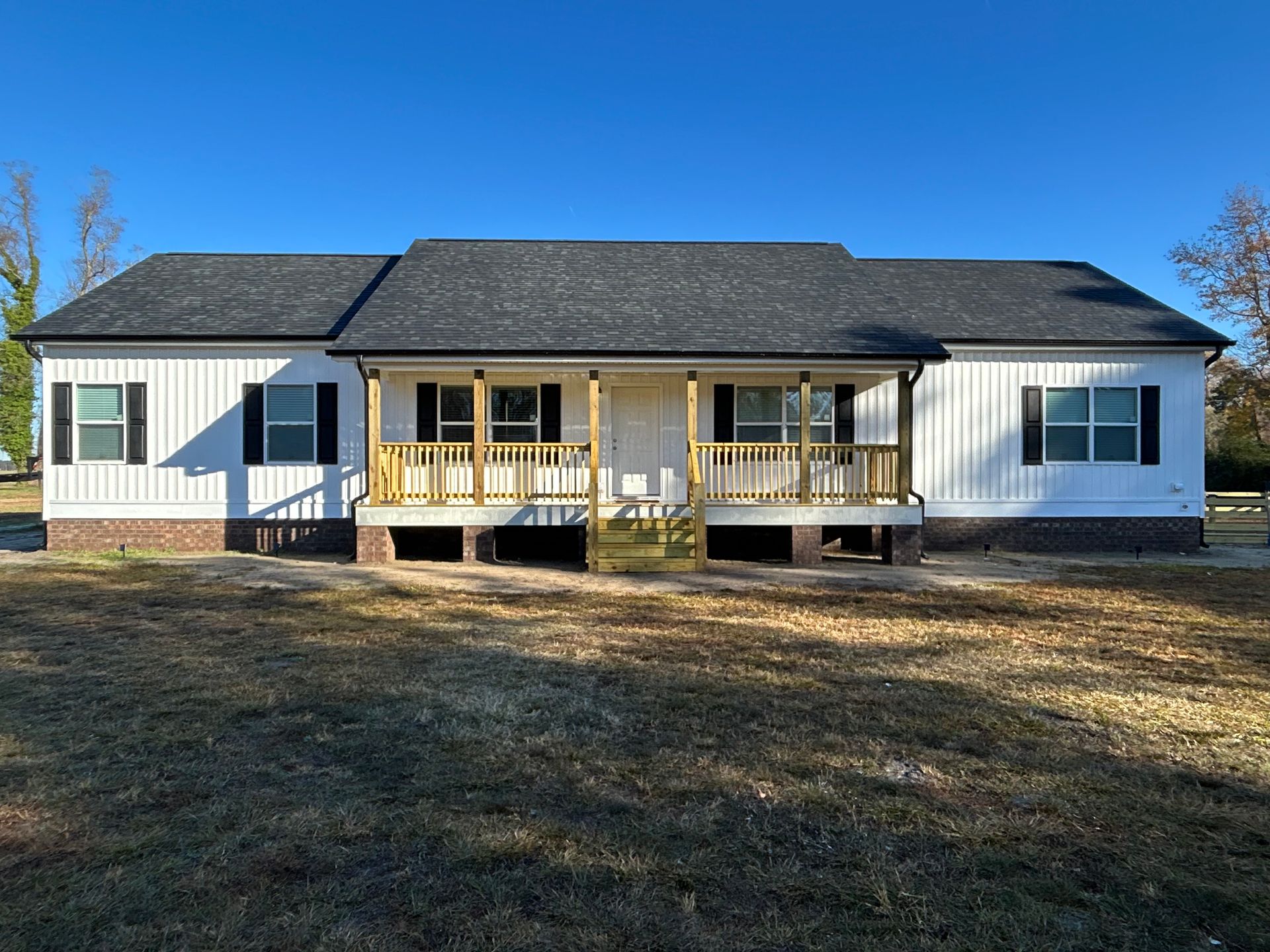 White house with black shutters, a small porch, and a dark roof under a clear blue sky.
