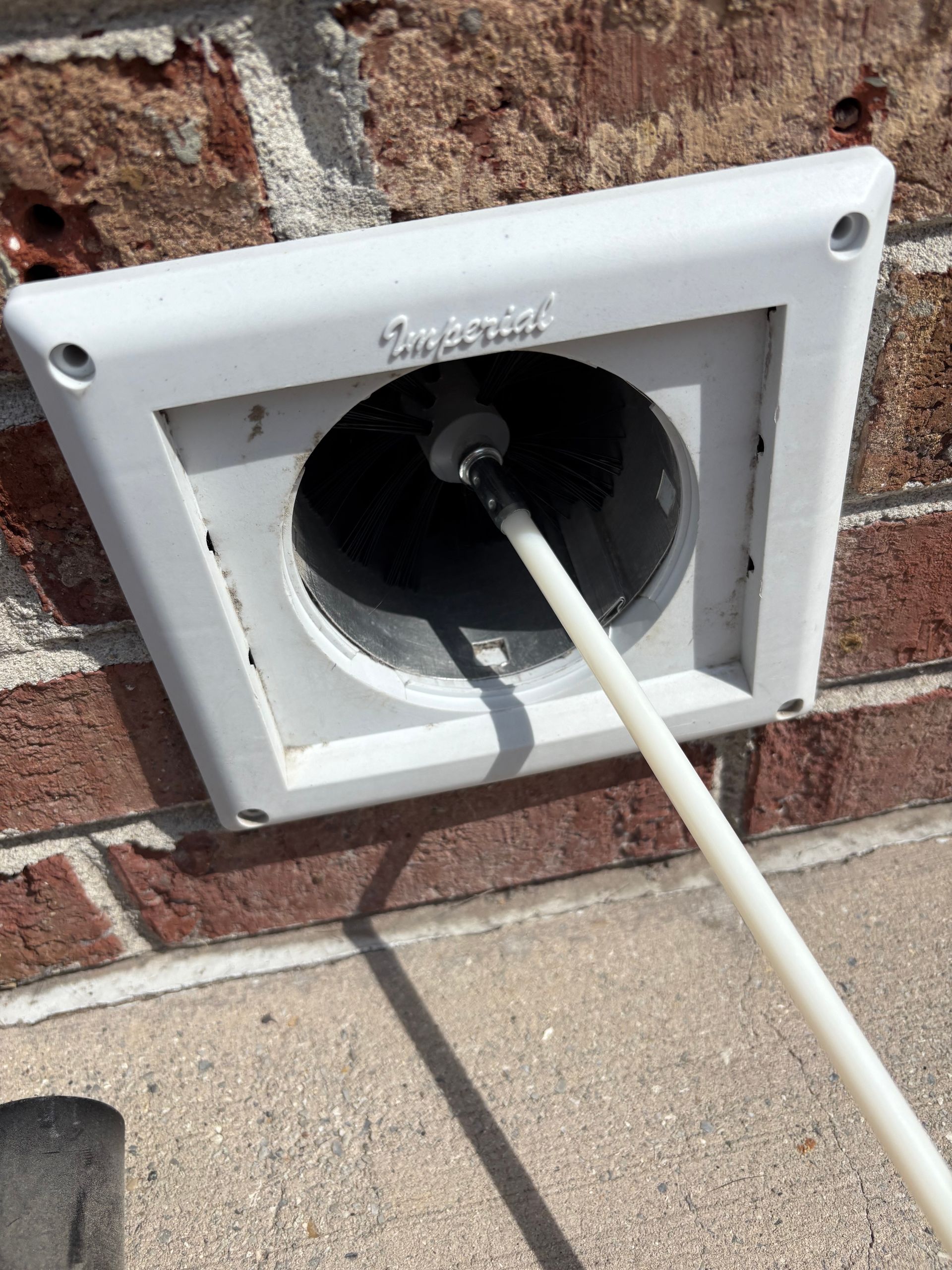 White dryer vent on a brick wall, cleaning rod inserted into the vent.