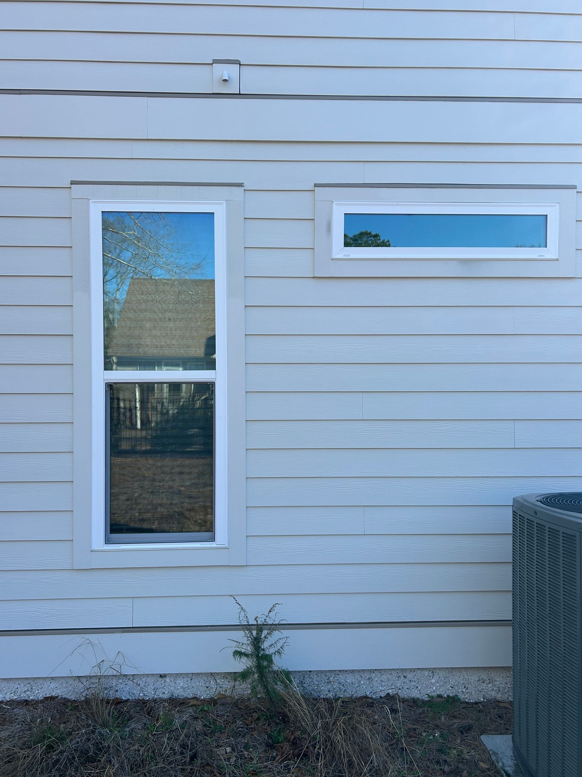Two windows on a light gray house with horizontal siding; an air conditioning unit is in the bottom right.