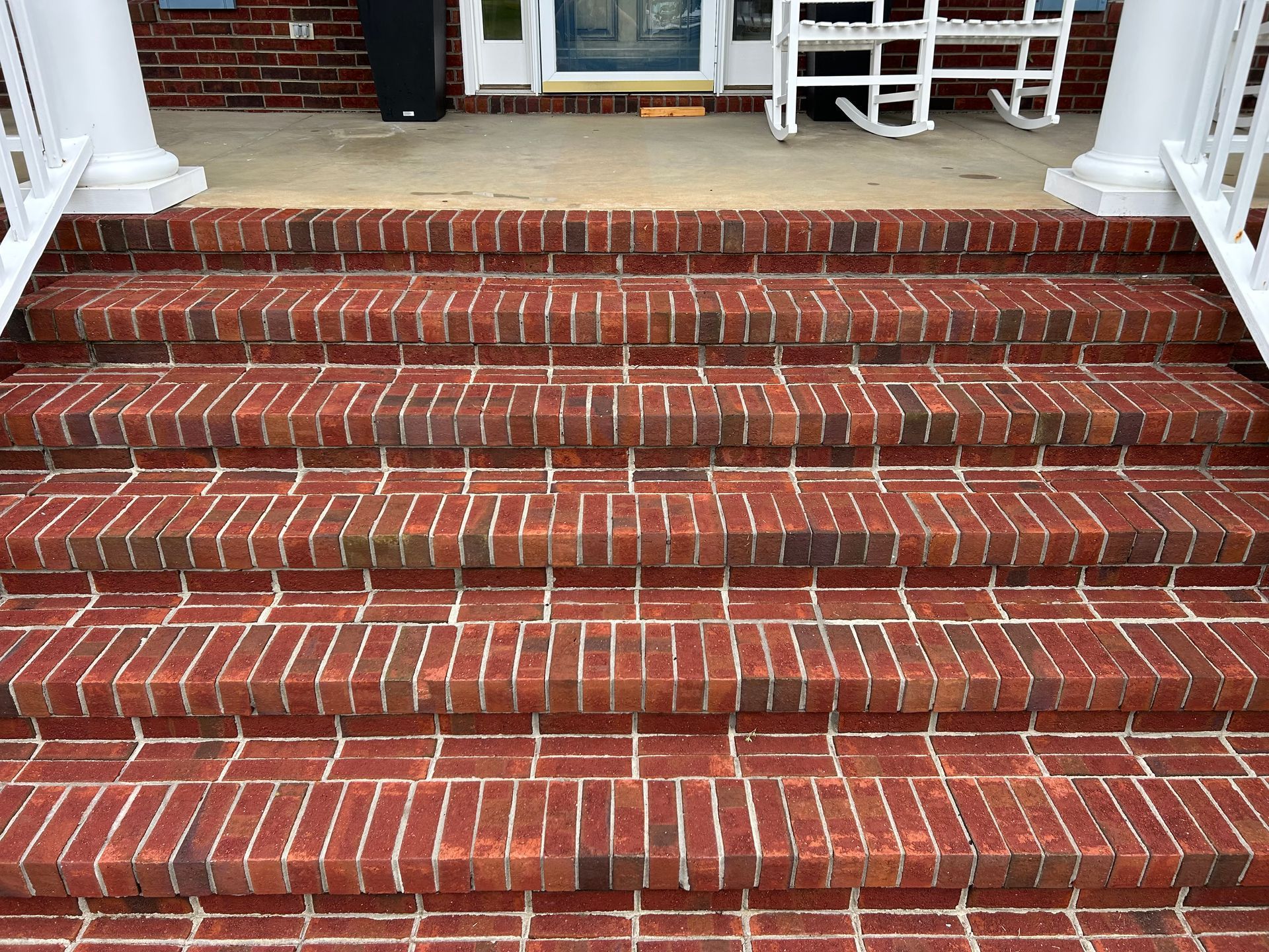 Brick steps leading up to a porch with white columns and a rocking chair.
