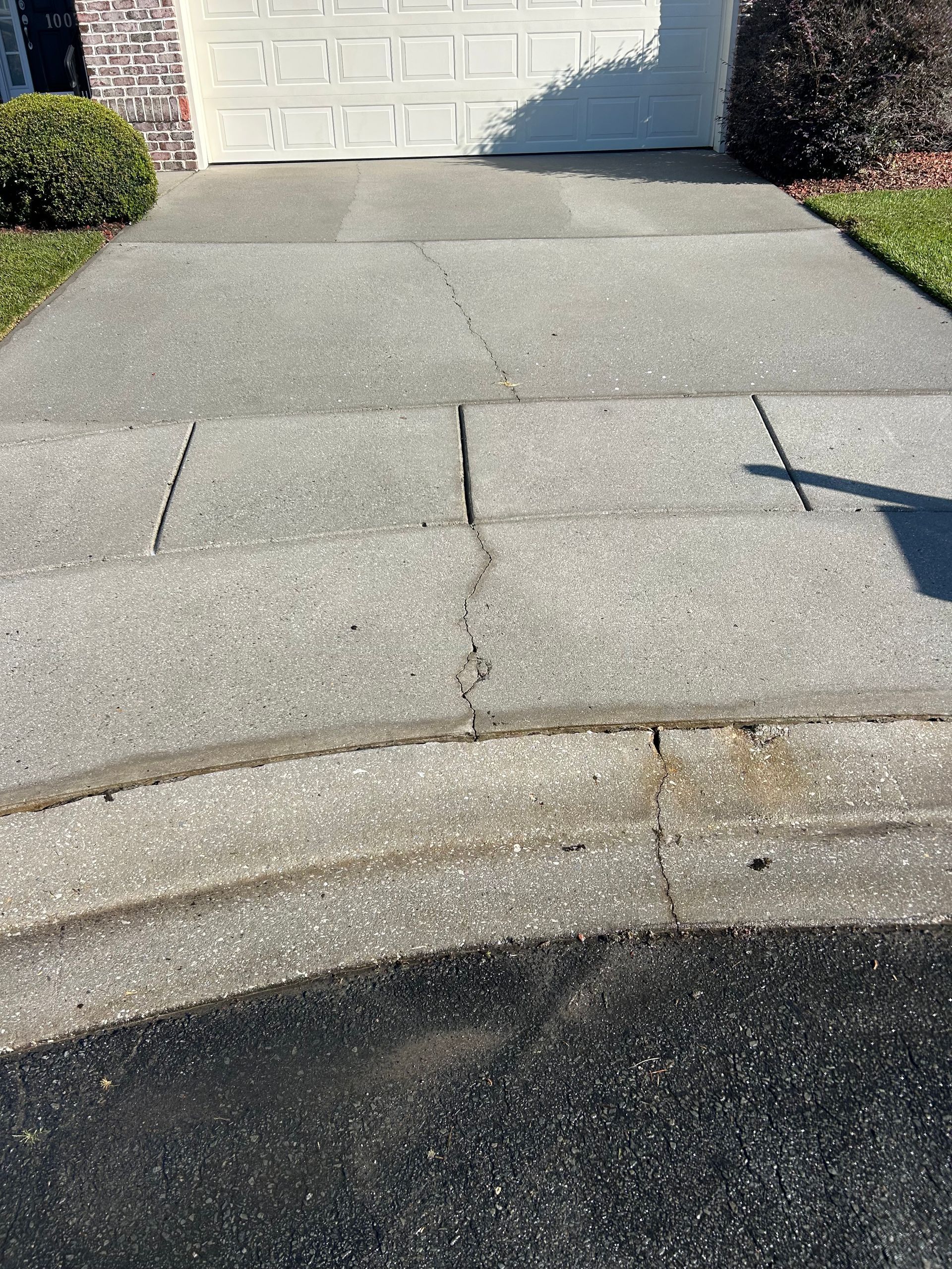 Concrete driveway with cracks, leading to a garage door.